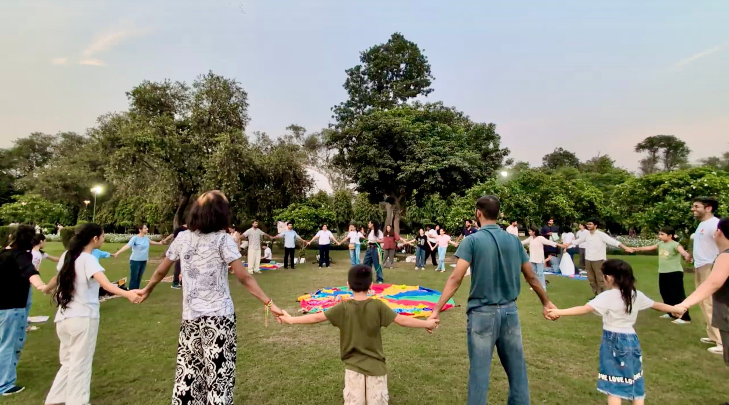 Participants holding hands in a large circle on the lawn at Lodhi Garden as the sun sets