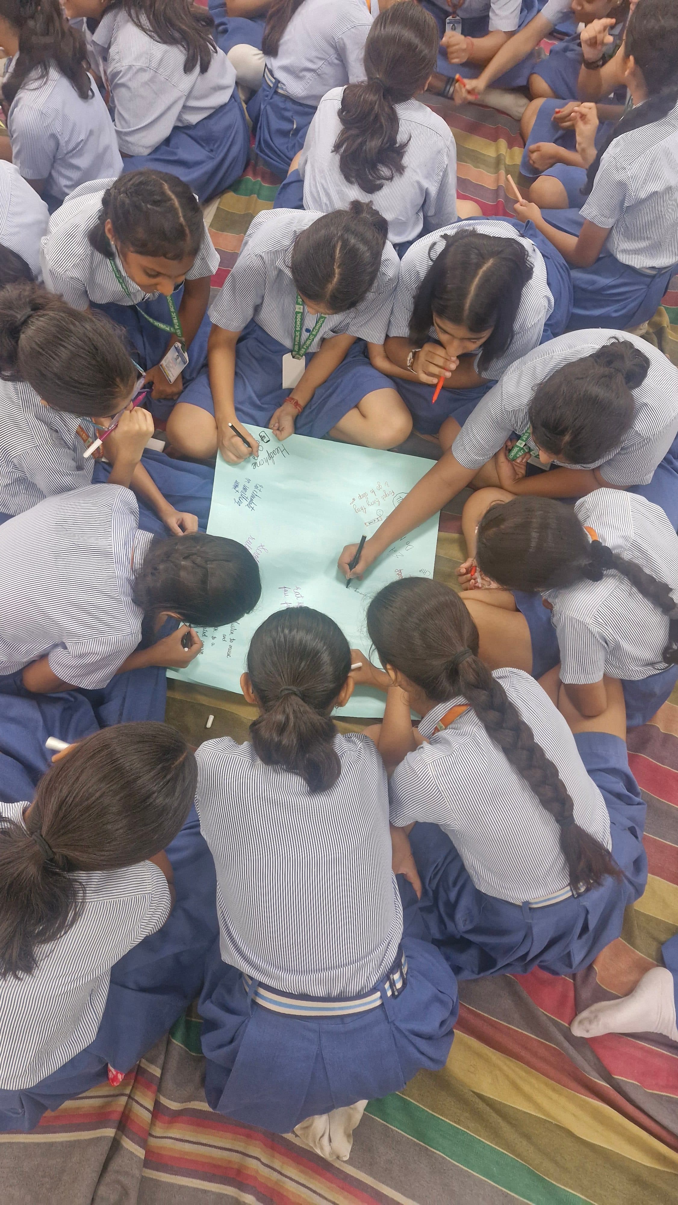 Schoolchildren in uniform crowded around a large sheet of paper, writing together during the exam stress session