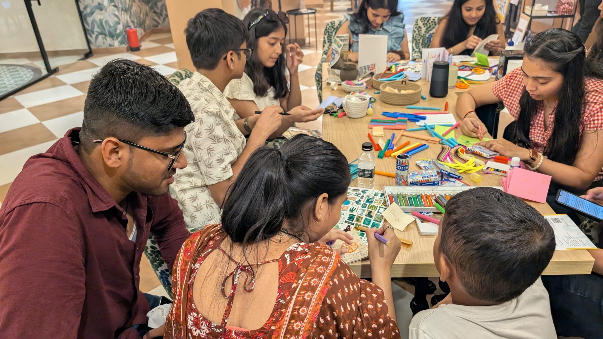 Participants crafting zines around a cafe table covered in markers, crayons and paper